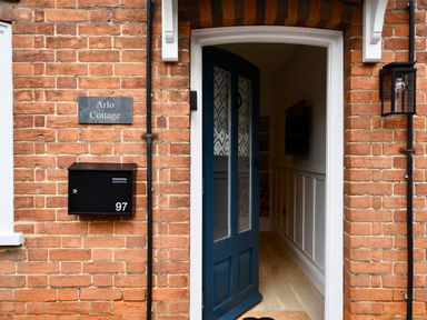 A brick house entrance with a black door partially open a black mailbox with number 97 and a sign saying Arlo Cottage at Arlo Cottage Orford