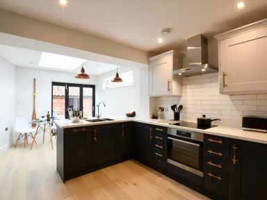 A kitchen with black lower cabinets white upper cabinets and a dining area with glass table and white chairs at Arlo Cottage Orford