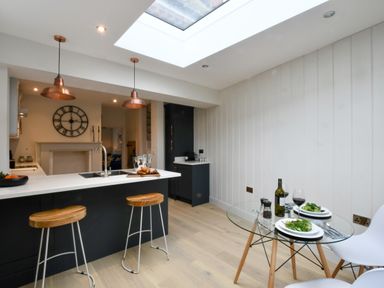 A kitchen with a black island and wooden stools with a glass dining table and two white chairs at Arlo Cottage Orford