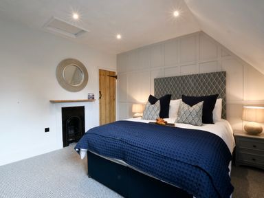 A bedroom with a bed with patterned headboard and blue bedding a wooden door and a round mirror above a fireplace at Arlo Cottage Orford