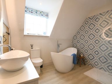 A bathroom with a freestanding bathtub a toilet a sink and a patterned tiled wall at Arlo Cottage Orford