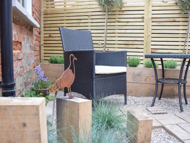 An outdoor seating area with a wicker chair and table on a gravel surface at Arlo Cottage in Orford
