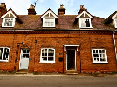A brick cottage exterior with white framed windows and two doors on a street at Arlo Cottage Orford