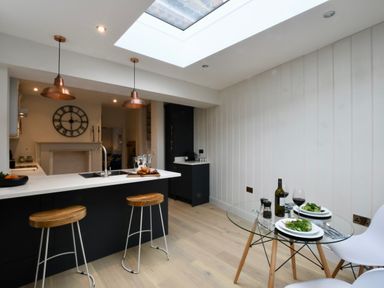 A kitchen with black cabinets wooden stools a glass dining table and white chairs at Arlo Cottage Orford
