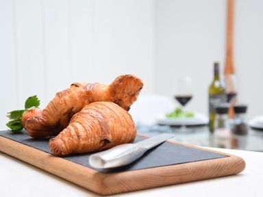 Two croissants and a strawberry on a wooden cutting board with a knife in a dining area at Arlo Cottage Orford