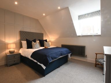 A bedroom with a double bed with patterned headboard and navy bedding two bedside tables with lamps and a window with patterned blind at Arlo Cottage Orford