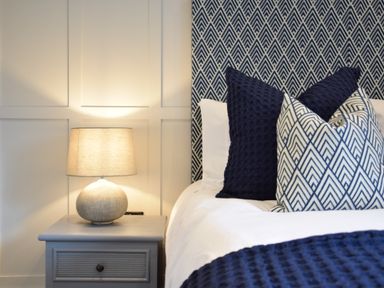A bedside table with a lamp next to a bed with patterned pillows and a textured headboard at Arlo Cottage Orford
