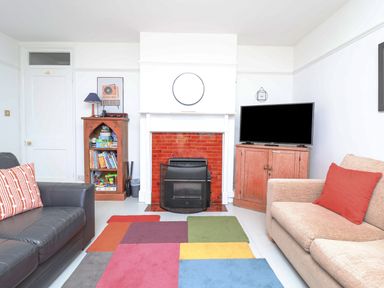 A living room with a fireplace a television on a cabinet and a colorful rug at Time Out Southwold in Southwold