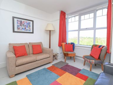 A living room with a beige sofa red pillows two armchairs colorful patchwork rug and a large window at Time Out Southwold in Southwold