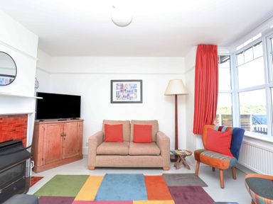 A living room with a sofa and red cushions a multicolored rug and a colorful chair at Time Out Southwold in Southwold