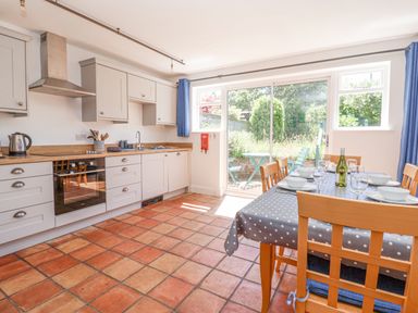 A kitchen with wooden cabinets a dining table with chairs set for a meal and sliding glass doors leading to a garden at Time Out Southwold in Southwold