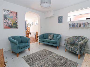 A living room with two blue armchairs a blue sofa a rug and a bookshelf with DVDs at Time Out Southwold in Southwold
