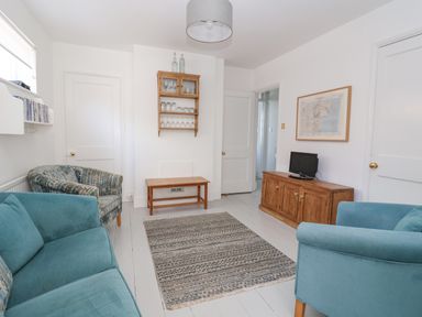 A living room with blue armchairs and sofa a wooden cabinet with a small TV and a wall-mounted shelf with glasses at Time Out Southwold in Southwold
