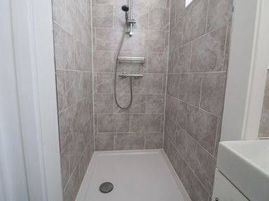 A tiled shower area with a showerhead a drain and part of a white sink at Time Out Southwold in Southwold