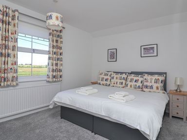 A bedroom with a double bed featuring printed cushions and curtains with beach huts at Time Out Southwold