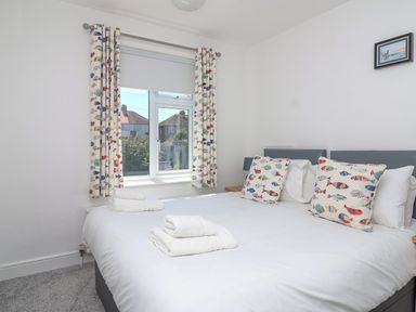 A bedroom with a bed featuring fish-patterned cushions and curtains and folded towels on the bed at Time Out Southwold in Southwold
