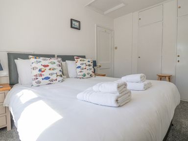 A bedroom with a double bed with white linens and fish patterned pillows at Time Out Southwold in Southwold