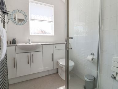 A bathroom with a sink, toilet, shower enclosure, and storage cabinets at Time Out Southwold in Southwold