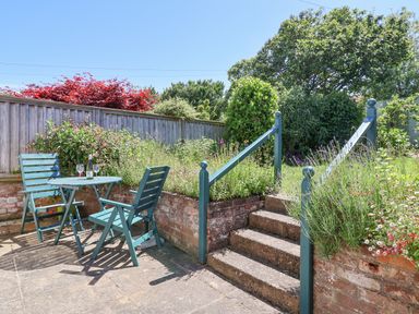 A garden patio with two wooden chairs and a table next to steps leading to a raised grassy area at Time Out Southwold in Southwold