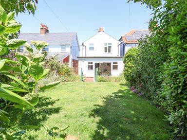 A garden with grass and bushes leading to a white two-story house with a glass door extension at Time Out Southwold in Southwold