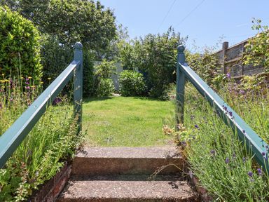 A garden with green grass and plants on both sides of stone steps with blue railings