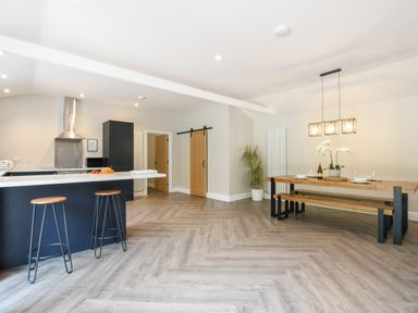 A kitchen with a breakfast bar and stools next to a dining table with bench seating at The Piglets in Newbourne Near Woodbridge
