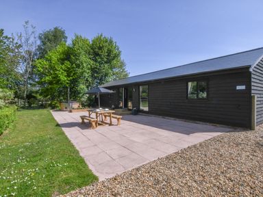 An outdoor patio area with a picnic table and umbrella next to a black wooden building at The Piglets in Newbourne Near Woodbridge