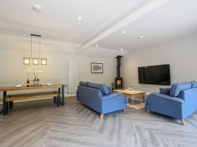 A living room with blue sofas a wall mounted television a wood burning stove and a dining table at The Piglets in Newbourne Near Woodbridge