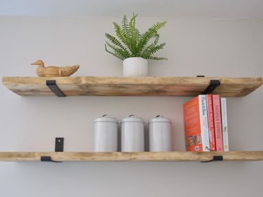 Two wooden shelves mounted on a wall with a wooden duck and a potted plant on the top shelf and three storage canisters and four books on the bottom shelf at The Piglets in Newbourne Near Woodbridge