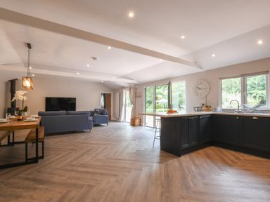 An open plan kitchen and living room with blue sofas wooden dining table and large windows at The Piglets in Newbourne Near Woodbridge