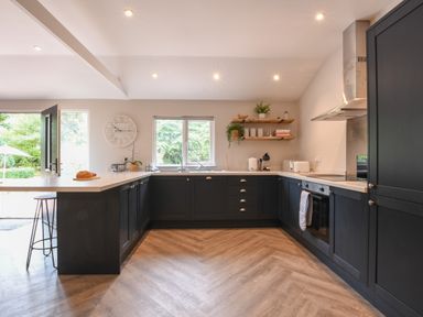 A kitchen with dark cabinets a stove a sink and shelves with plants and jars at The Piglets in Newbourne Near Woodbridge
