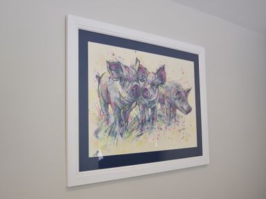 A framed painting of three pigs on a wall at The Piglets in Newbourne Near Woodbridge