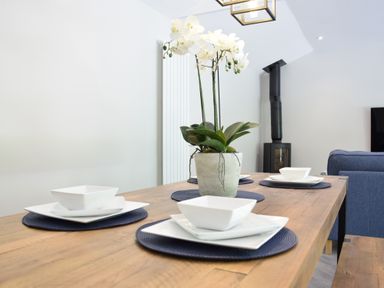 A dining table with white plates and bowls on blue placemats and a potted orchid at The Piglets in Newbourne Near Woodbridge