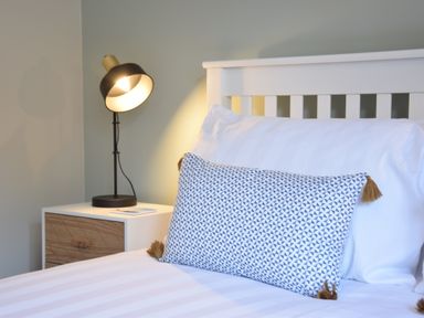 A bed with white bedding and a patterned pillow next to a bedside table with a black lamp at The Piglets in Newbourne Near Woodbridge