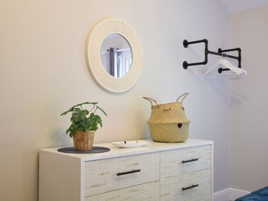 A dresser with a plant basket and a decorative basket under a round mirror and next to a wall mounted clothes rack at The Piglets in Newbourne Near Woodbridge