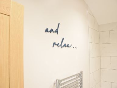 A bathroom wall with the words and relax on it and a towel radiator at The Piglets in Newbourne Near Woodbridge