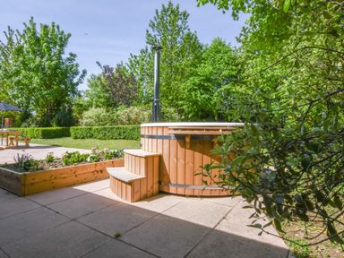 An outdoor space with a wooden hot tub and planter box surrounded by trees and greenery at The Piglets in Newbourne Near Woodbridge