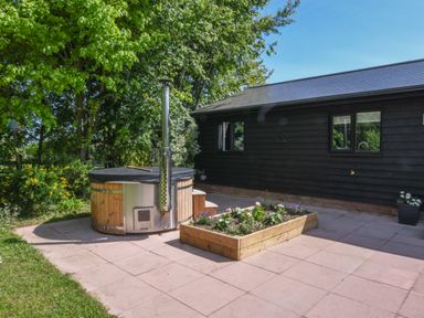 A patio with a hot tub and a raised garden bed next to a black wooden building at The Piglets in Newbourne Near Woodbridge