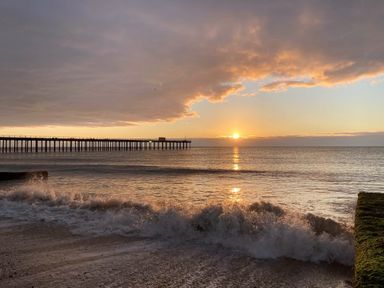 A sunset over the ocean with a long pier extending into the water and waves crashing on the shore at The Piglets in Newbourne Near Woodbridge