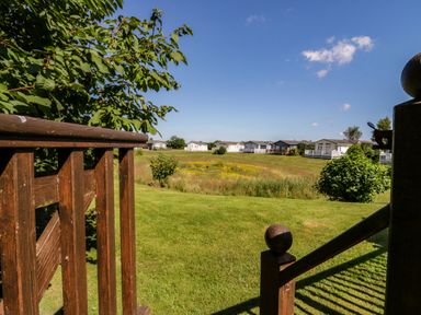 A grassy field with bushes and several small houses in the distance viewed from a wooden deck at The Hide Out in Aldeburgh