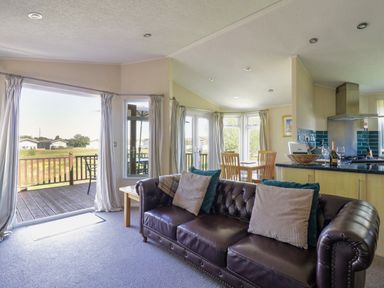 An open living space with a leather sofa, wooden dining table and kitchen area with blue tiles at The Hide Out Aldeburgh