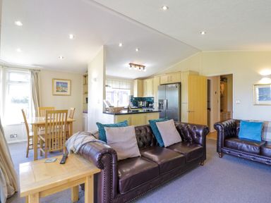 A living room with two leather sofas and a wooden dining table adjacent to a kitchen with light wood cabinets at The Hide Out, Aldeburgh