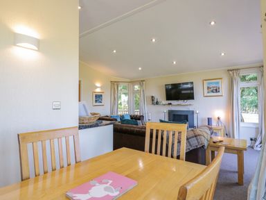 A dining area with wooden table and chairs adjacent to a living room with sofas and a wall-mounted TV at The Hide Out in Aldeburgh