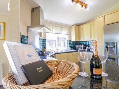 A kitchen with wooden cabinets a stainless steel refrigerator a wicker basket with books and a bottle of prosecco with two wine glasses on the counter at The Hide Out Aldeburgh