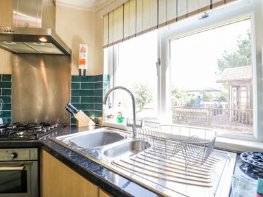A kitchen sink with a drying rack next to a window showing an outdoor view at The Hide Out in Aldeburgh