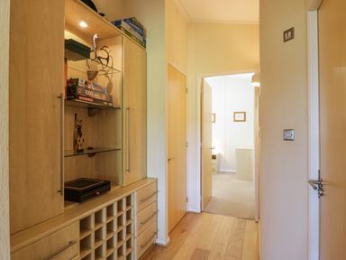 A hallway with wooden floor and built-in wooden cabinet with shelves housing board games and decorative items at The Hide Out in Aldeburgh