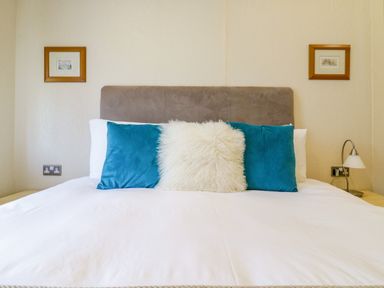 A bed with white sheets and blue and white pillows in a bedroom with framed pictures on the wall at The Hide Out in Aldeburgh