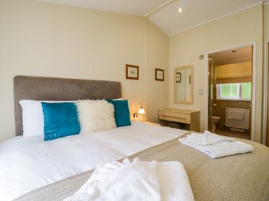 A bedroom with a bed with pillows and towels on it a small desk with a mirror and a door leading to a bathroom at The Hide Out in Aldeburgh