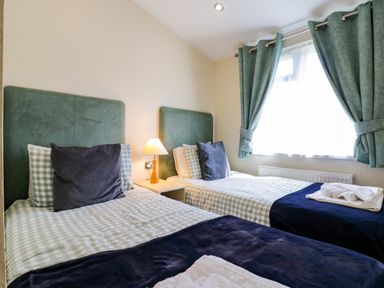 A bedroom with two single beds with green headboards a bedside table with a lamp and green curtains at The Hide Out in Aldeburgh