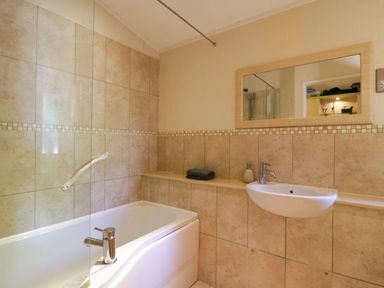 A bathroom with a bathtub a wall-mounted sink a mirror and beige tiled walls at The Hide Out Aldeburgh